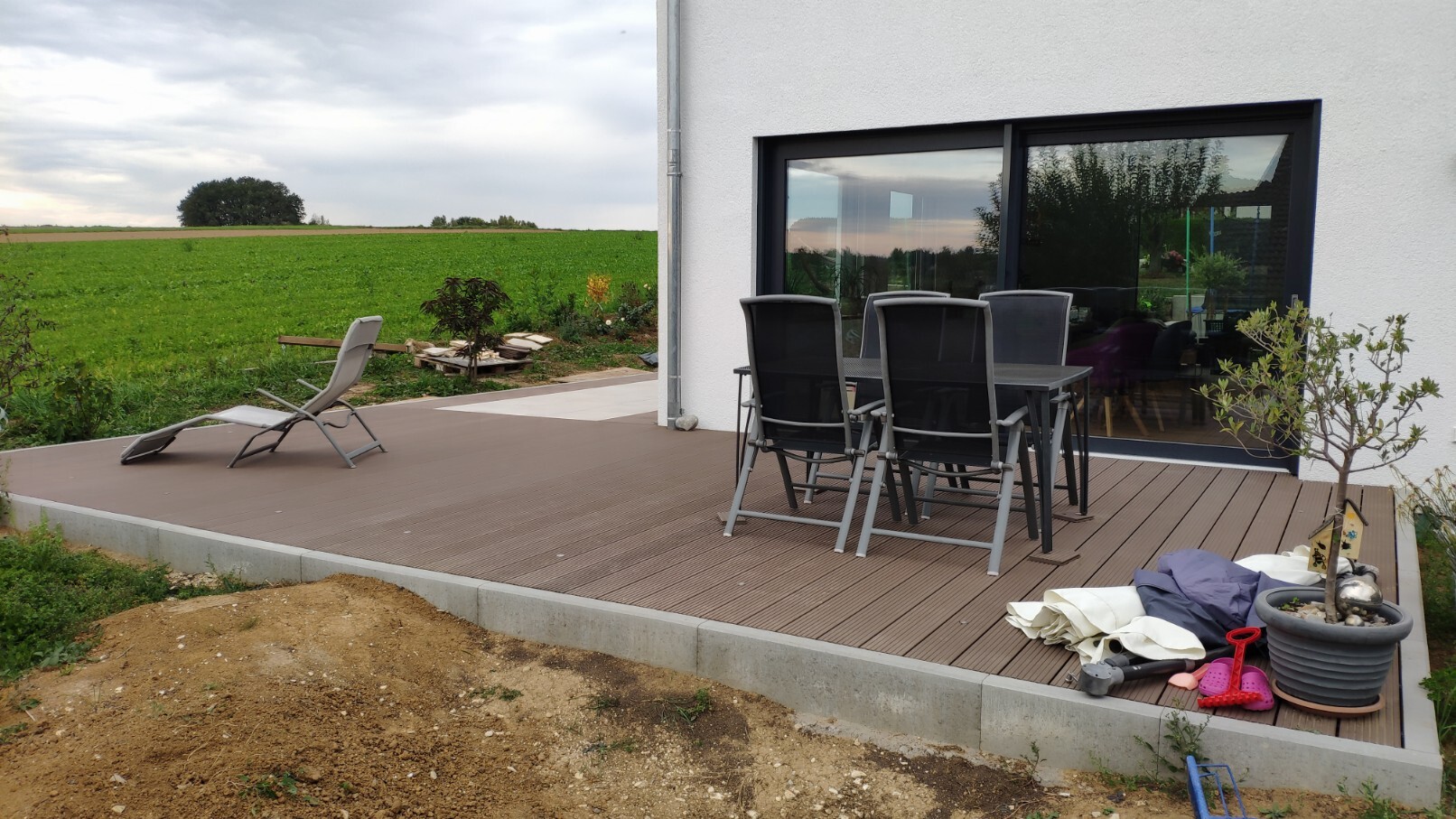Moderne Holzterrasse mit Esstisch und Stühlen vor Glasfront, Blick auf Felder.