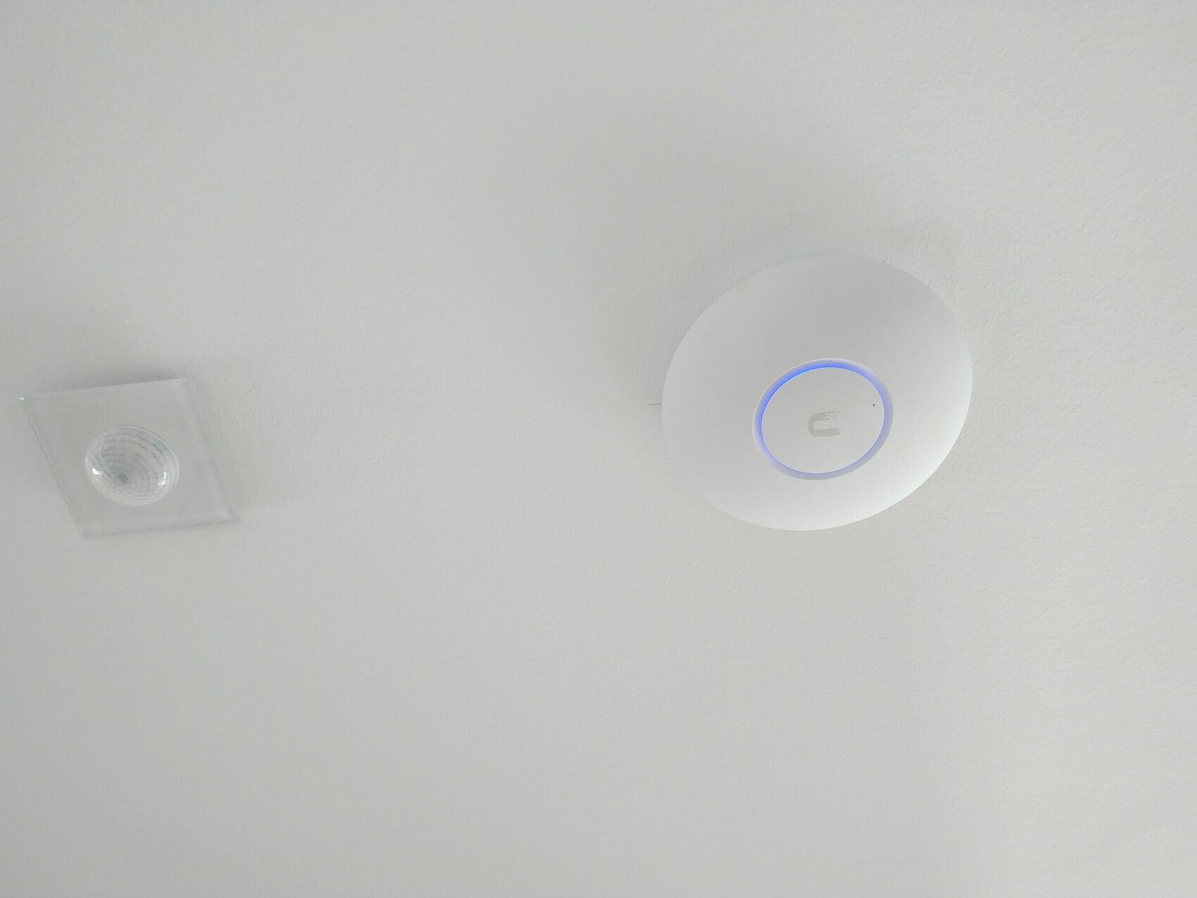 Weiße Decke mit rundem Sicherheitssensor und blauem Lichtring; links Deckeneinbauleuchte.