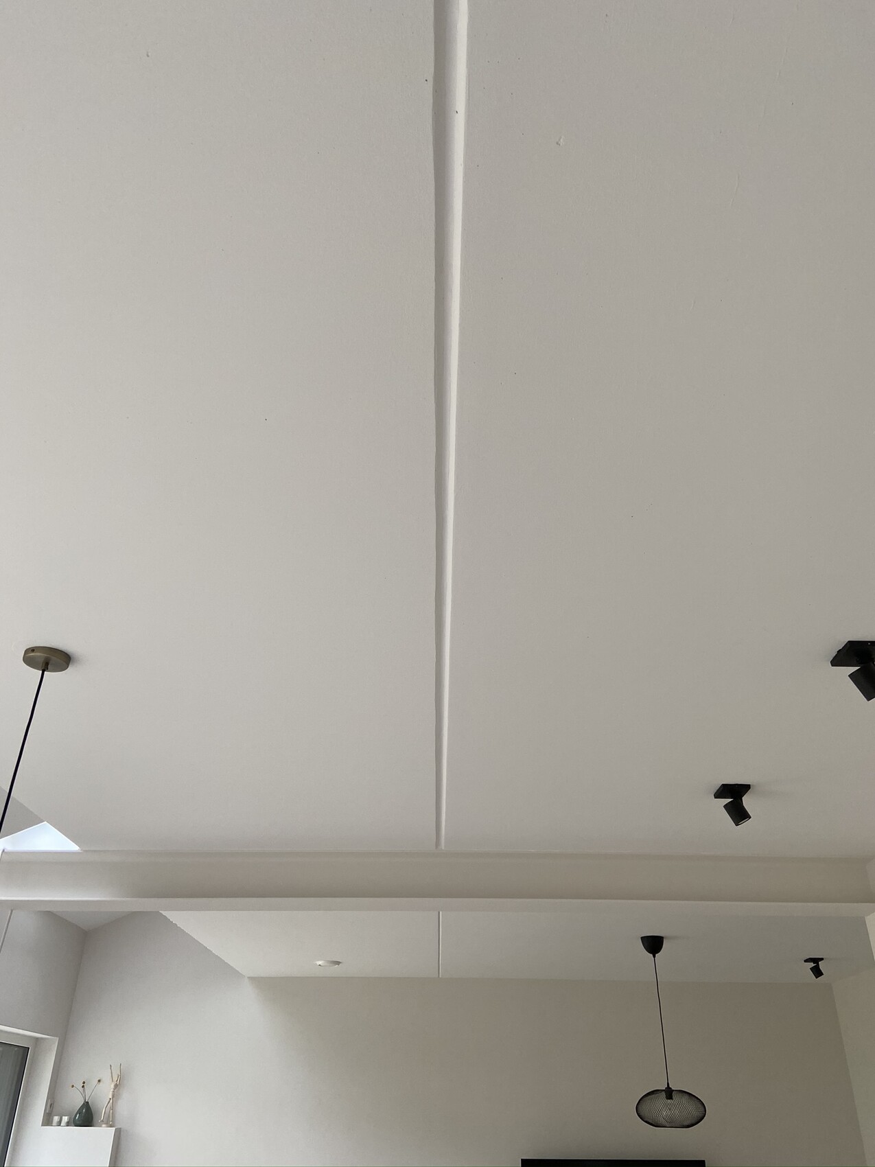 Weiße Decke mit zentraler Fuge, hängende Pendelleuchte und Deckenspots im offenen Wohnbereich.