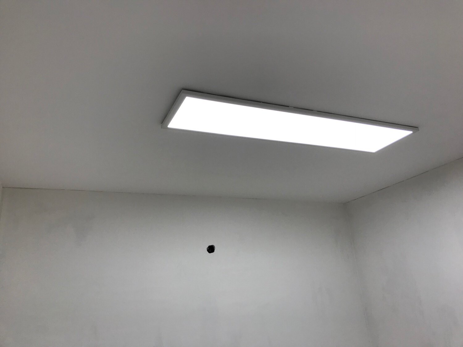 Weiße Decke mit einer rechteckigen Leuchte; Wand mit kleinem Loch.