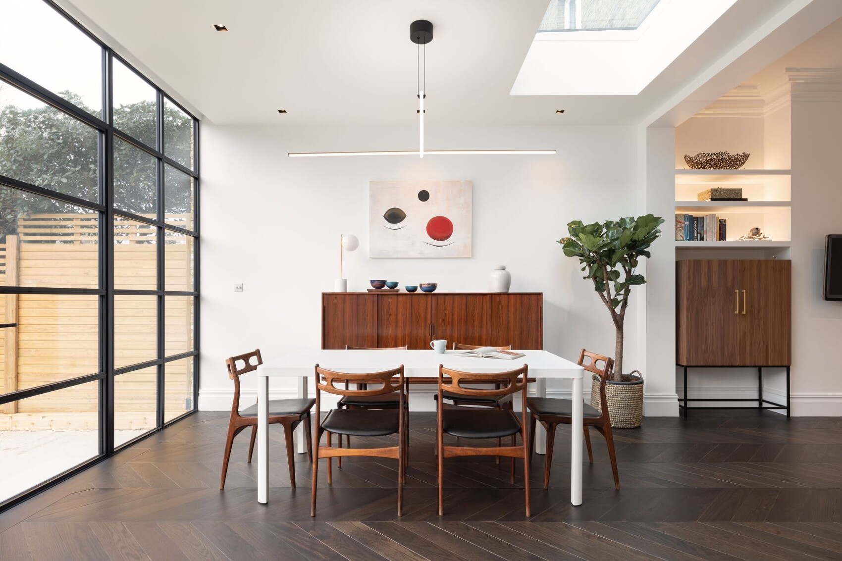 Helles modernes Esszimmer: weißer Tisch, Holzstühle, Sideboard, Pflanze und Fensterfront.