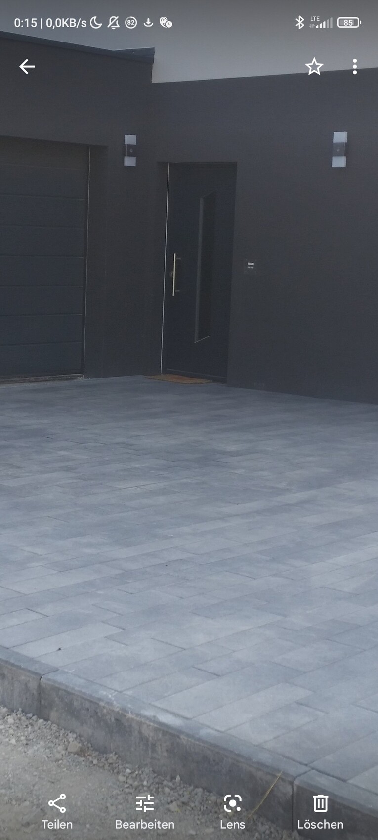 Moderne schwarze Hausfassade mit dunkler Eingangstür neben einer Garagentür; gepflasterter Vorhof