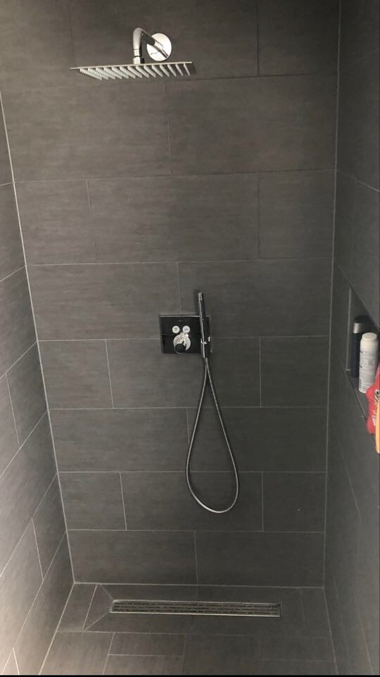Moderne Dusche: dunkle Fliesen, Decken-Duschkopf, Wandarmatur und Handbrause; Bodenrinne.