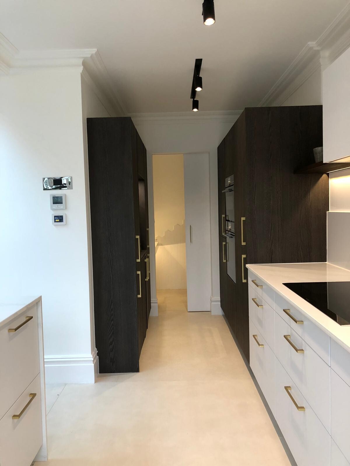 Moderne Galley-Küche mit dunklen Hochschränken rechts und links, weißen Unterschränken und goldenen Griffen.