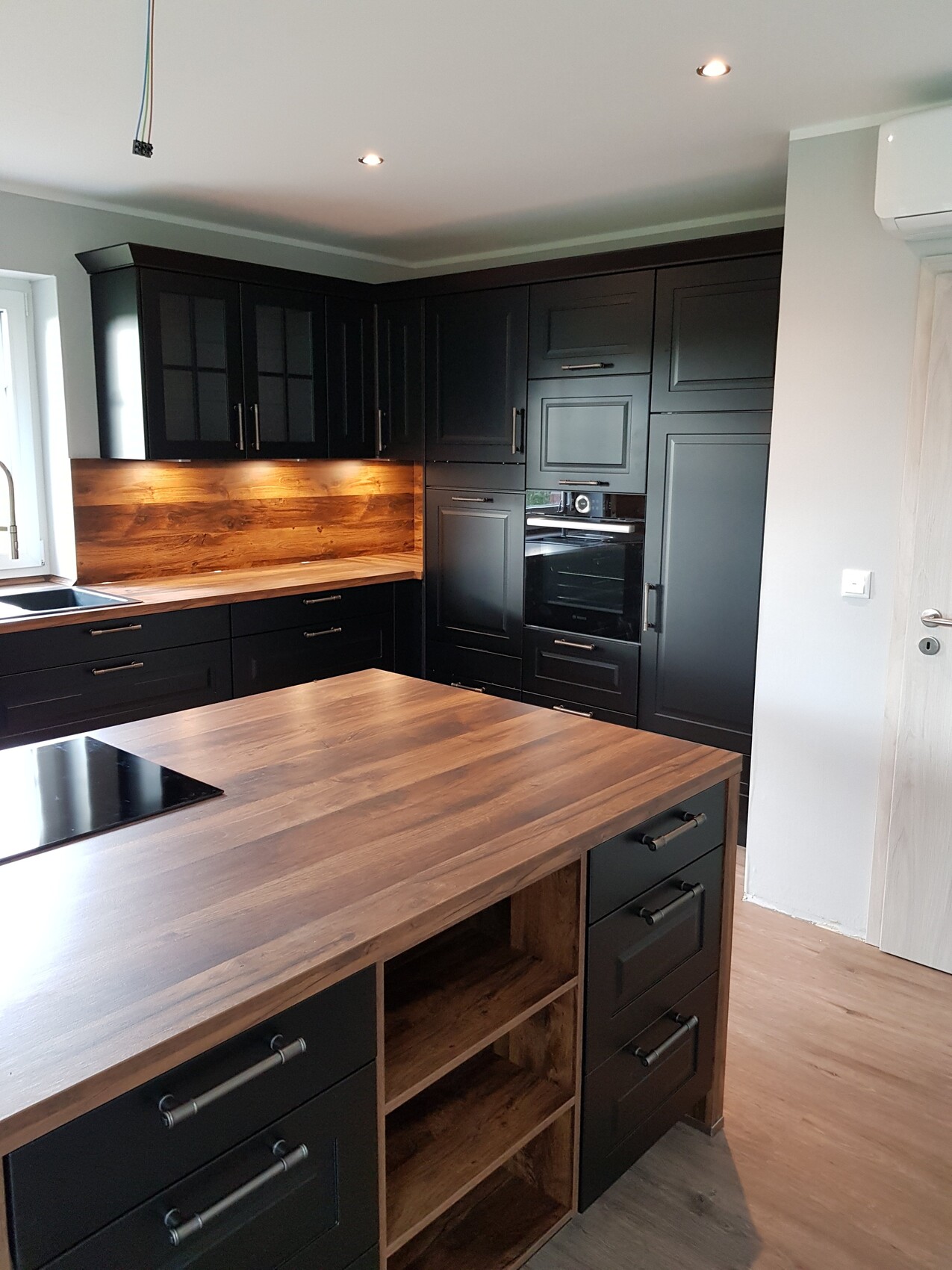 Moderne Küche mit schwarzen Fronten, Holz-Arbeitsplatten, Kücheninsel und Backofen.