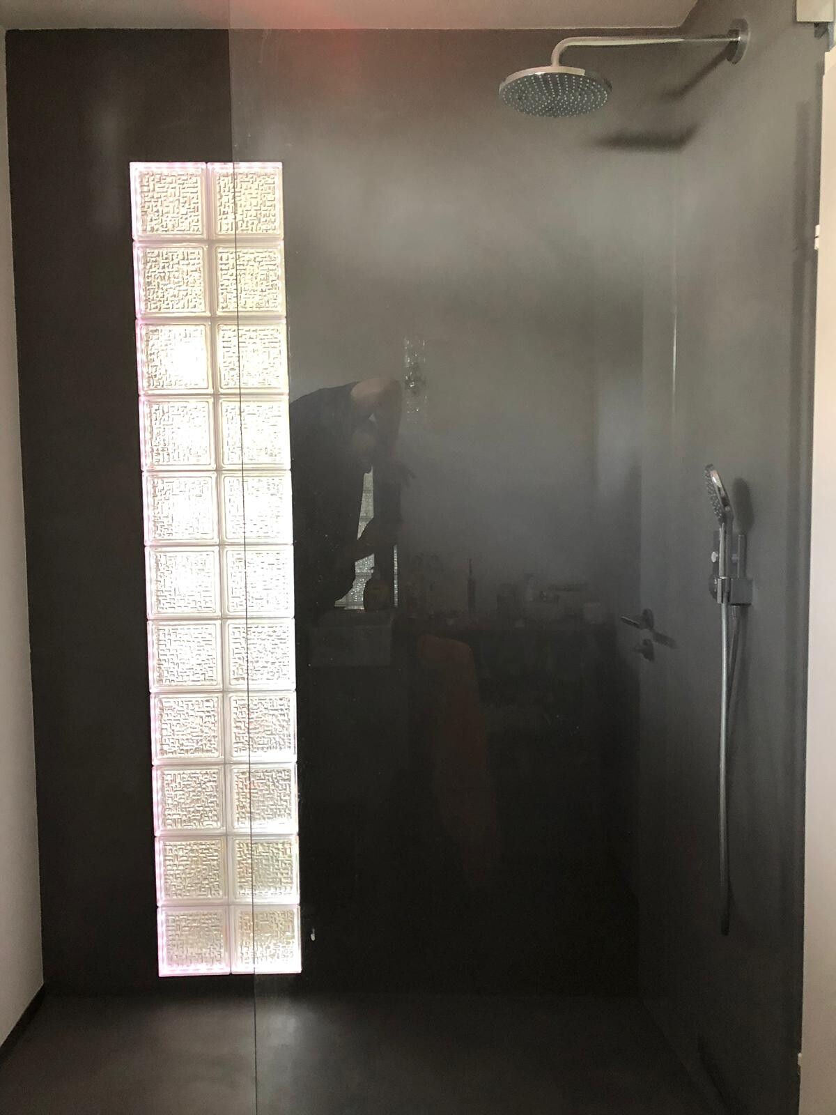 Dunkle Walk-in-Dusche mit Rundregenduschkopf oben, Glasblock-Säule links, Handbrause rechts.