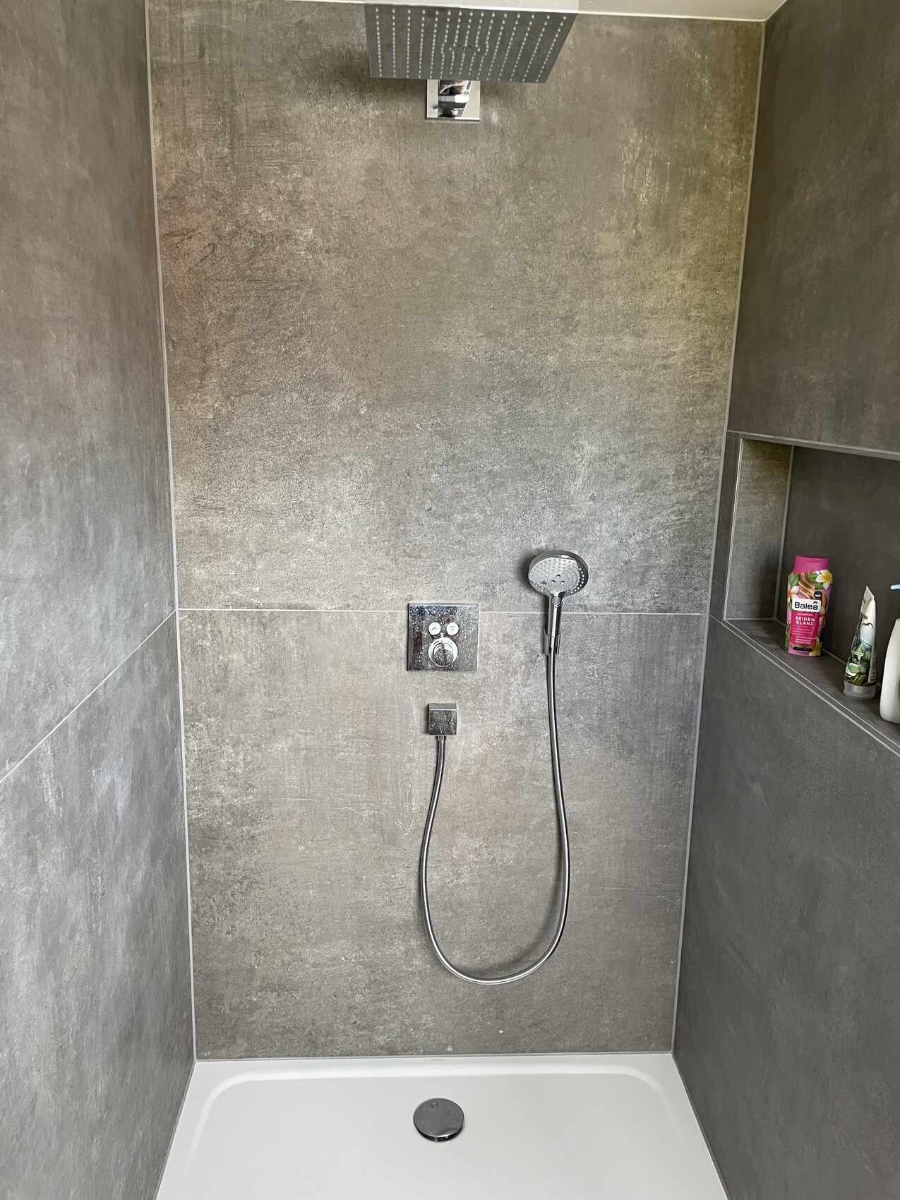 Moderner Duschbereich mit grauen Fliesen, Decken-Dusche, Handbrause und Ablage mit Pflegeprodukten.