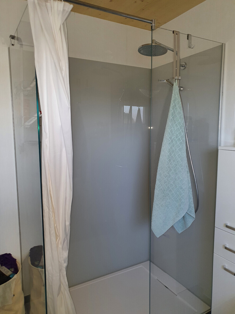 Moderne Glas-Dusche mit Regen-Duschkopf, weißem Vorhang und hellblauem Handtuch.