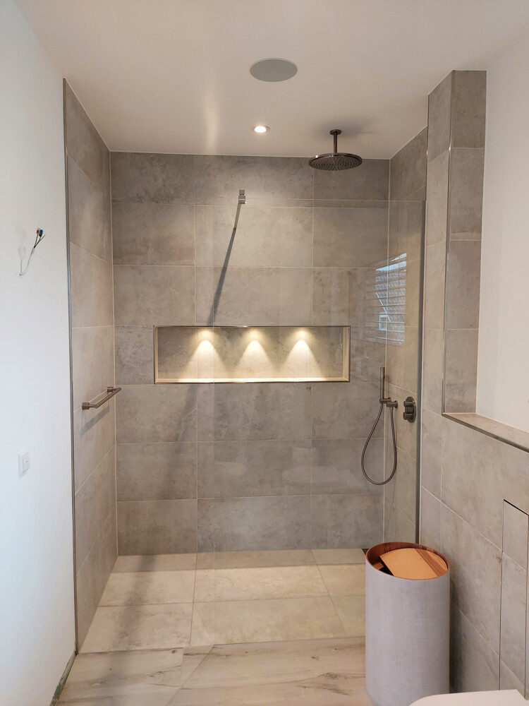 Große bodengleiche Dusche mit grauen Fliesen; Nische mit drei Downlights, Regenkopf und Handbrause.