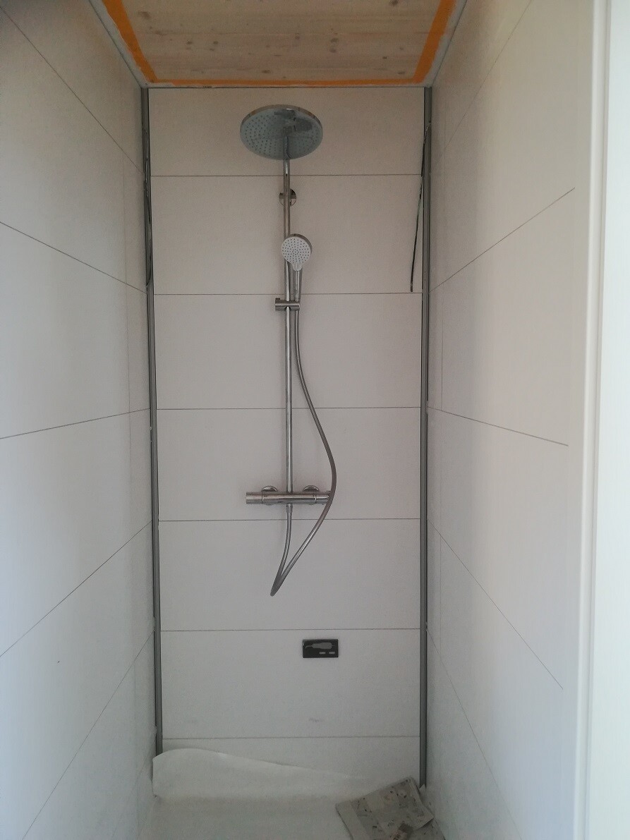Begehbare Duschkabine mit Deckenregendusche und Handbrause an verstellbarer Stange, weiße Fliesen.