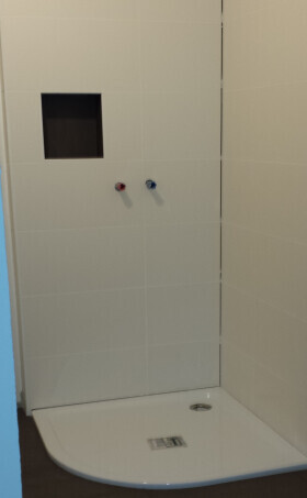 Helles Badezimmer mit Dusche, Wandnische und zwei Armaturen an der Wand über der Duschtasse