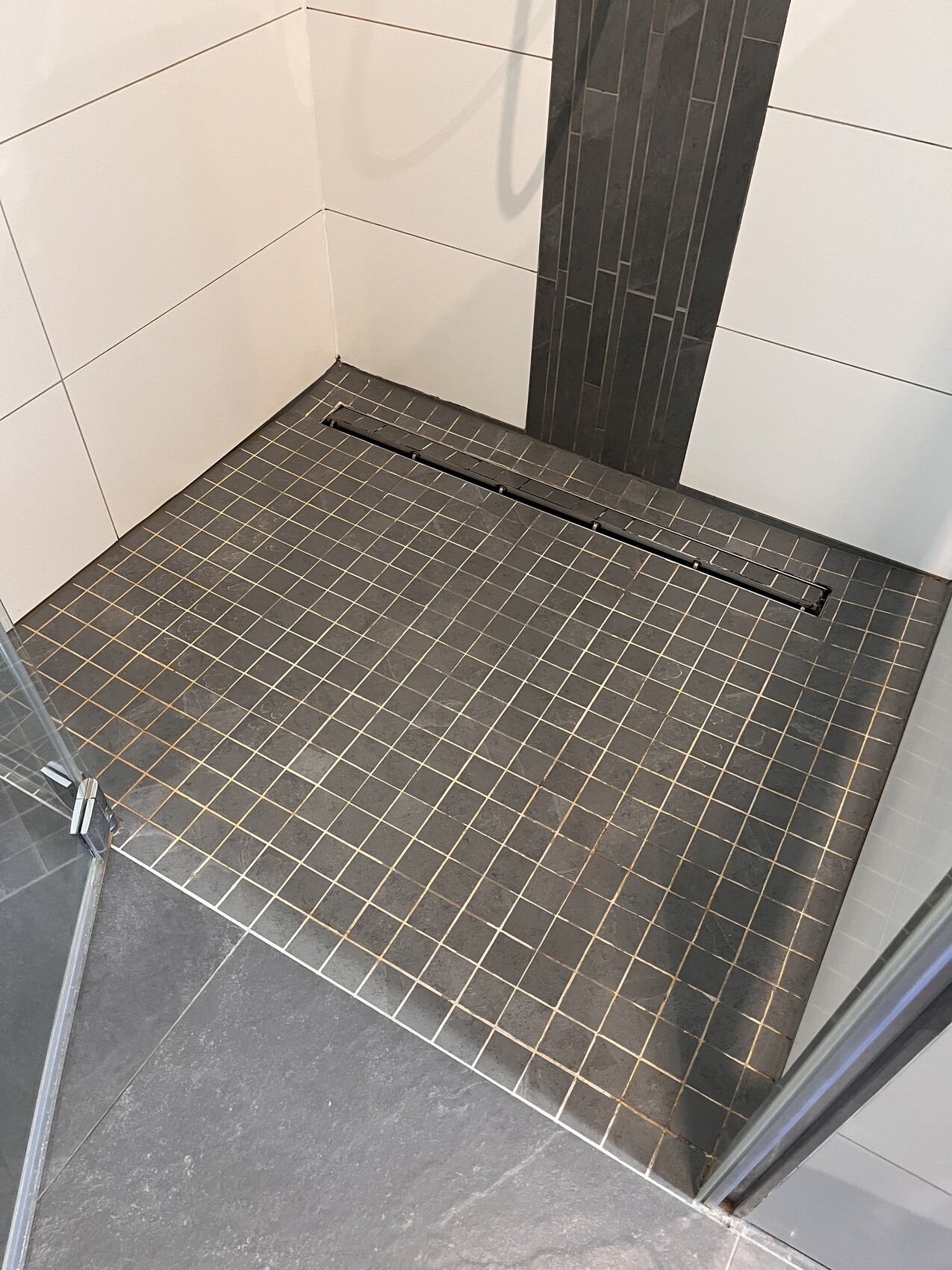 Duschkabine mit dunklem Fliesenboden, linearem Abfluss, weißen Wandfliesen.
