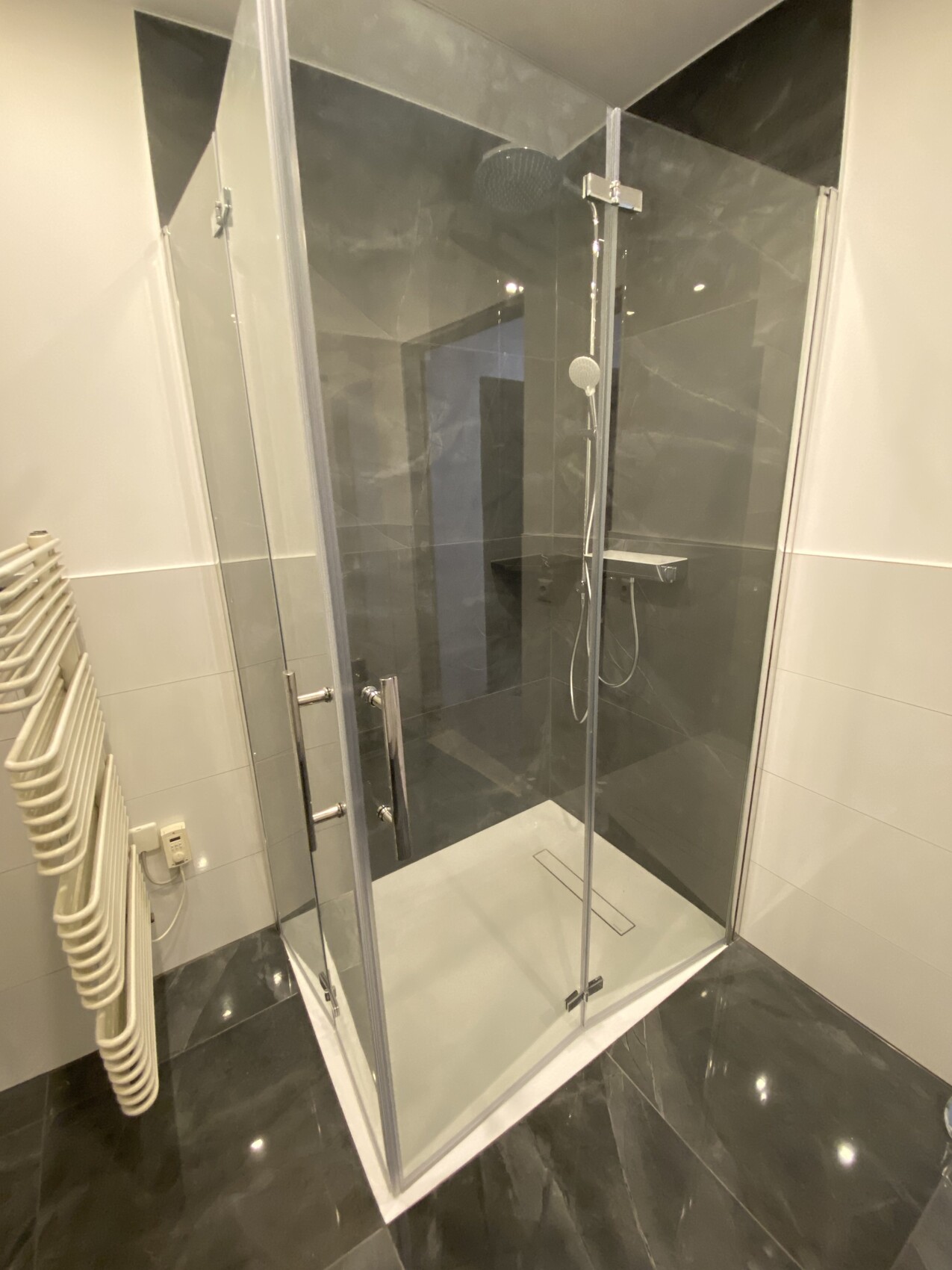 Moderne Glasdusche im Bad mit dunklen Fliesen und Handbrause