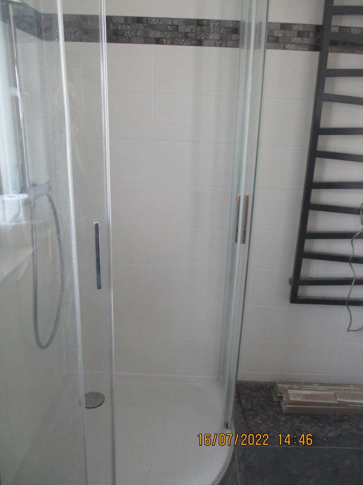 Moderne Glas-Duschkabine in einem Badezimmer, helle Fliesen und Heizkörper rechts.