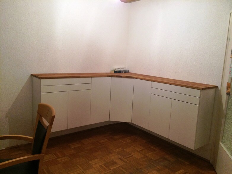 Küche in Ecke: weiße Unterschränke mit Holzarbeitsplatte, Holzfußboden, linker Stuhl.
