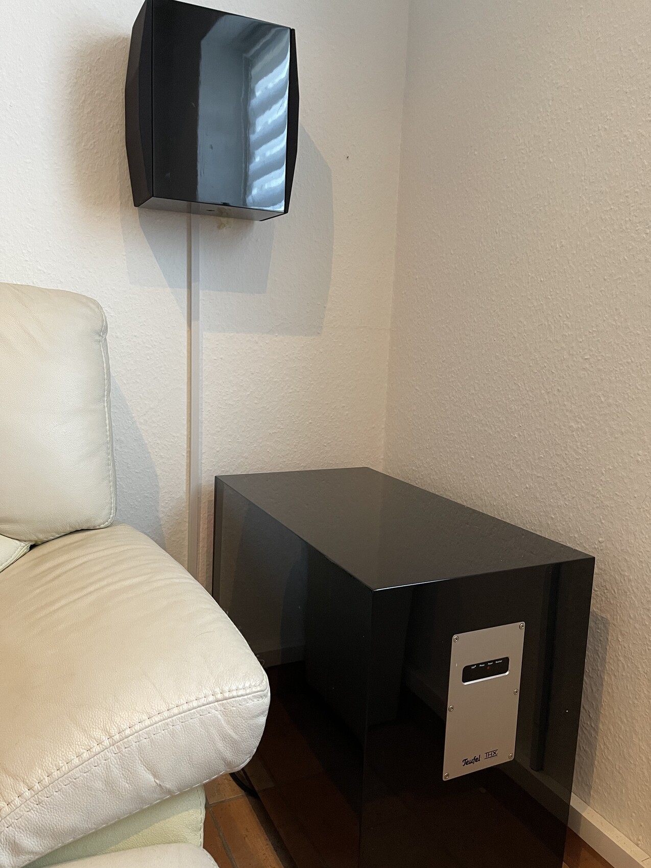 Schwarzer glänzender Beistelltisch neben cremefarbenem Ledersofa; Wandlautsprecher oben links.