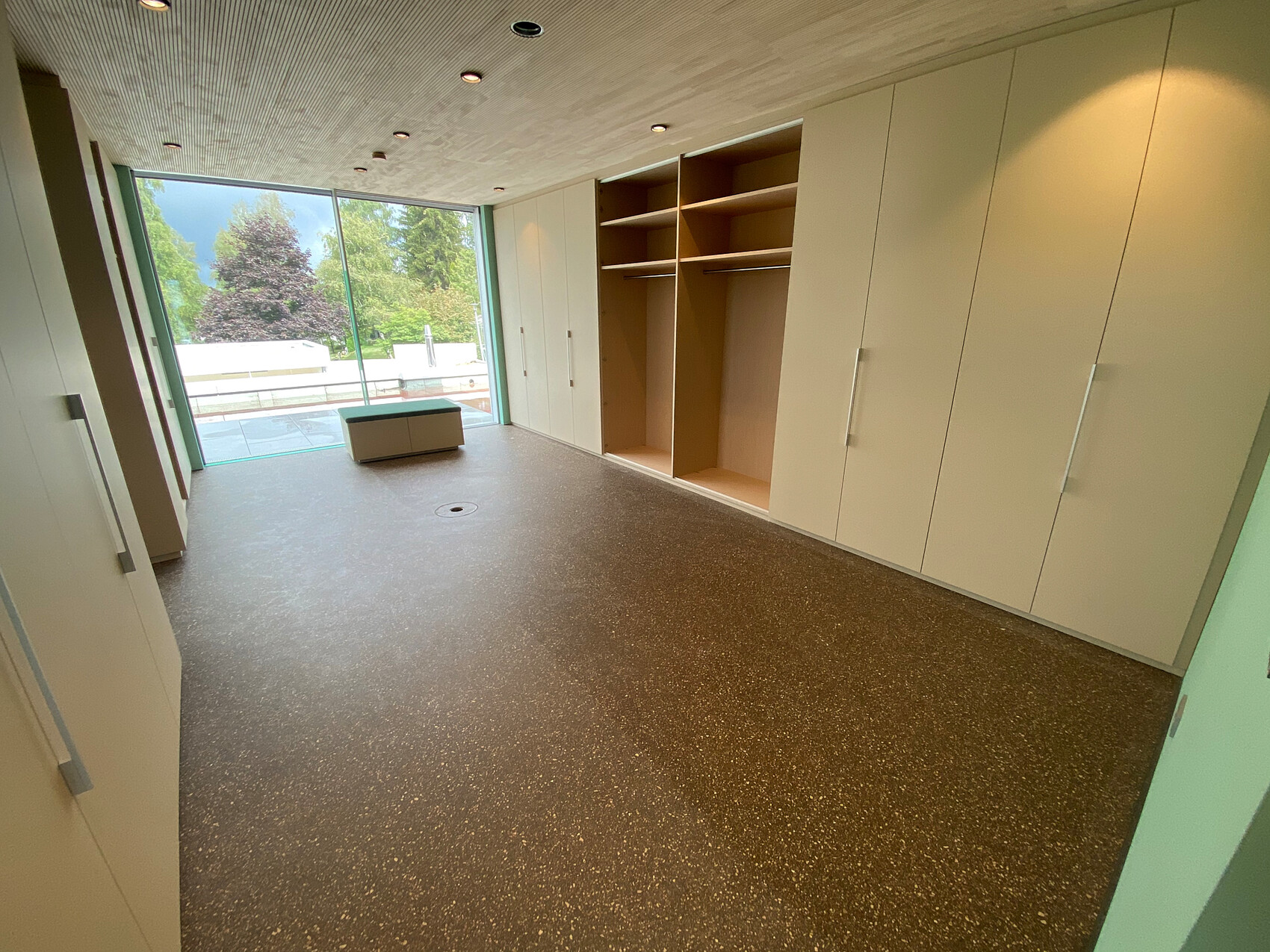 Moderner Ankleideraum mit weißen Schränken, offenen Regalen und Glasfront mit Gartenblick.