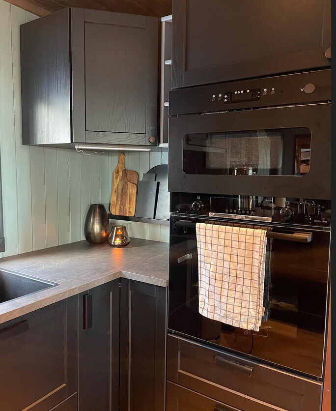Moderne Küche mit schwarzen Schränken, Backofen, Mikrowelle und Kerzenlicht auf der Arbeitsplatte.