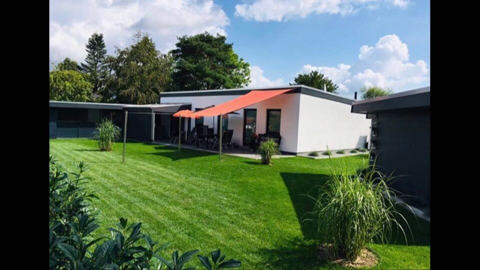 Moderne Einfamilienhaus-Garten mit orangefarbenem Sonnensegel über Terrasse und grünem Rasen.