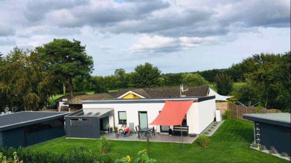 Modernes weißes Einfamilienhaus mit Terrasse, rotem Sonnensegel, Garten und Sitzecke.