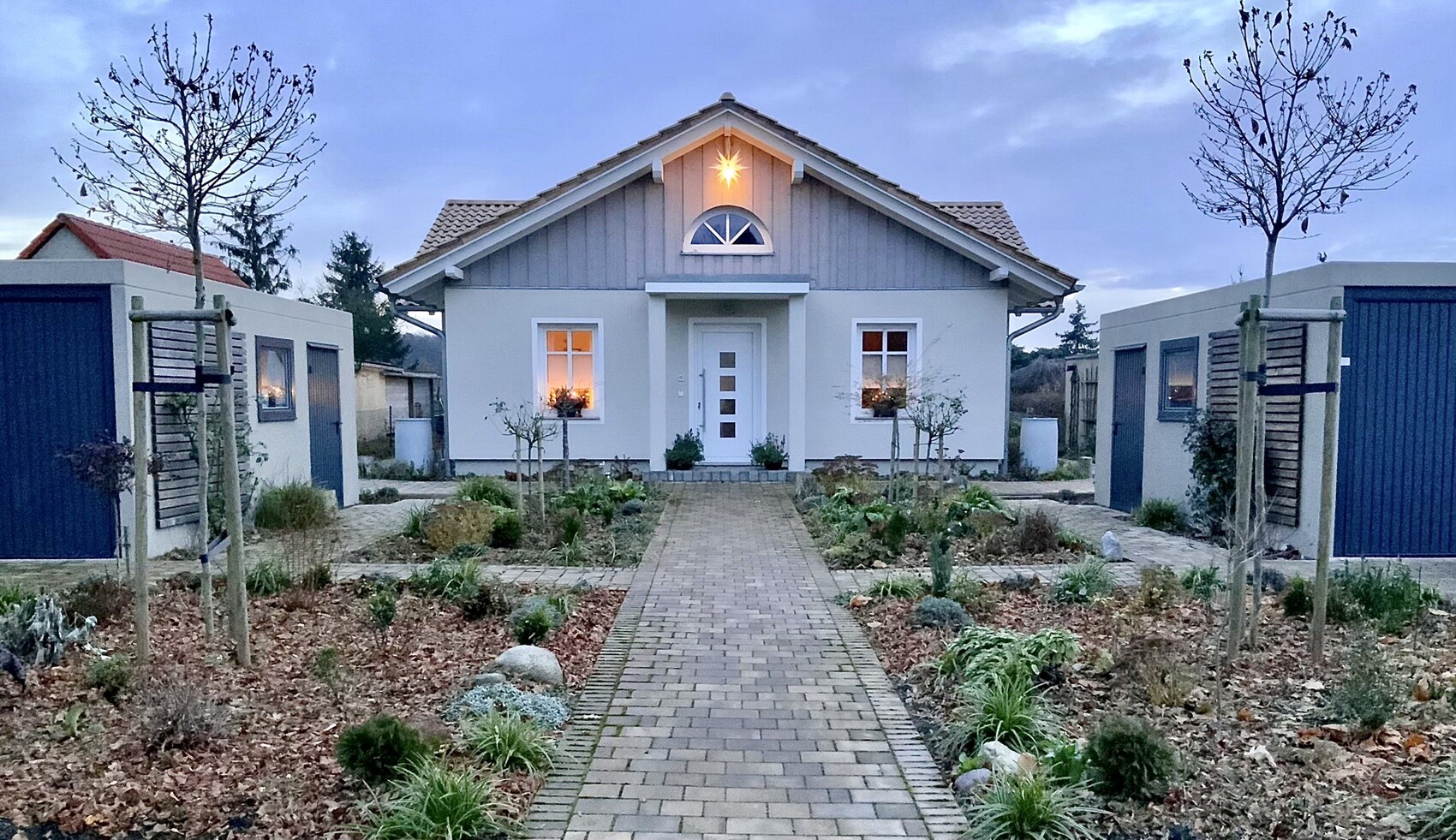 Hellblaues Einfamilienhaus mit Giebeldach, zentraler Tür, seitlichen Garagen und Gartenweg.