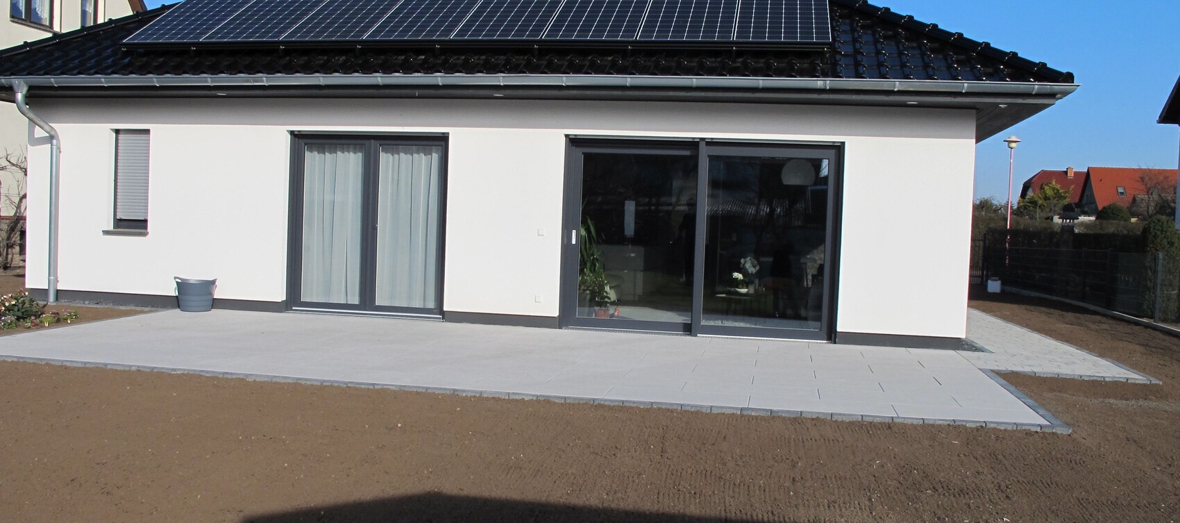Modernes Einfamilienhaus mit Solardach, Glas-Schiebetüren und Terrasse aus hellen Fliesen.