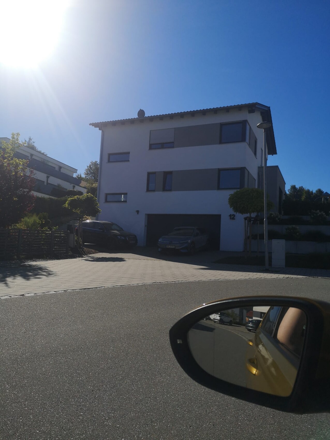 Moderne dreigeschossige Wohnhausfront mit Garage und Parkplätzen an sonnigem Tag
