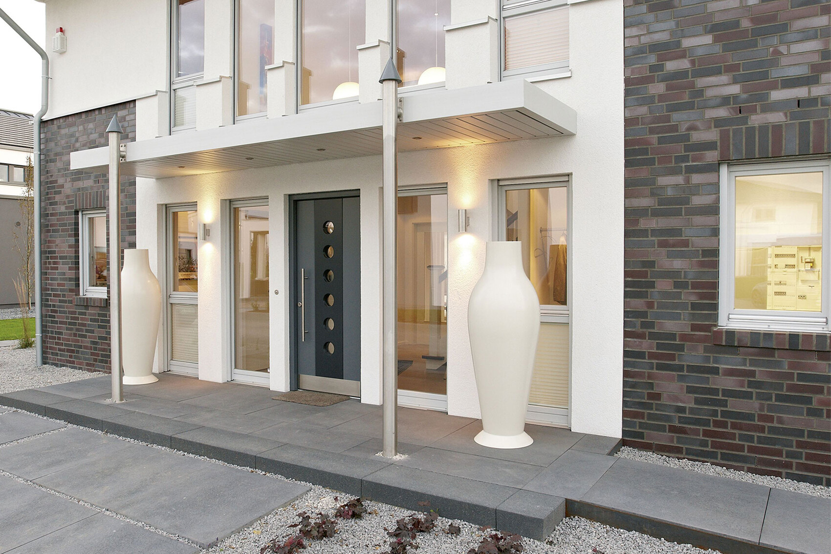 Moderne Hausfront mit dunkler Tür, Glasfenstern und zwei großen weißen Designvasen am Eingang.