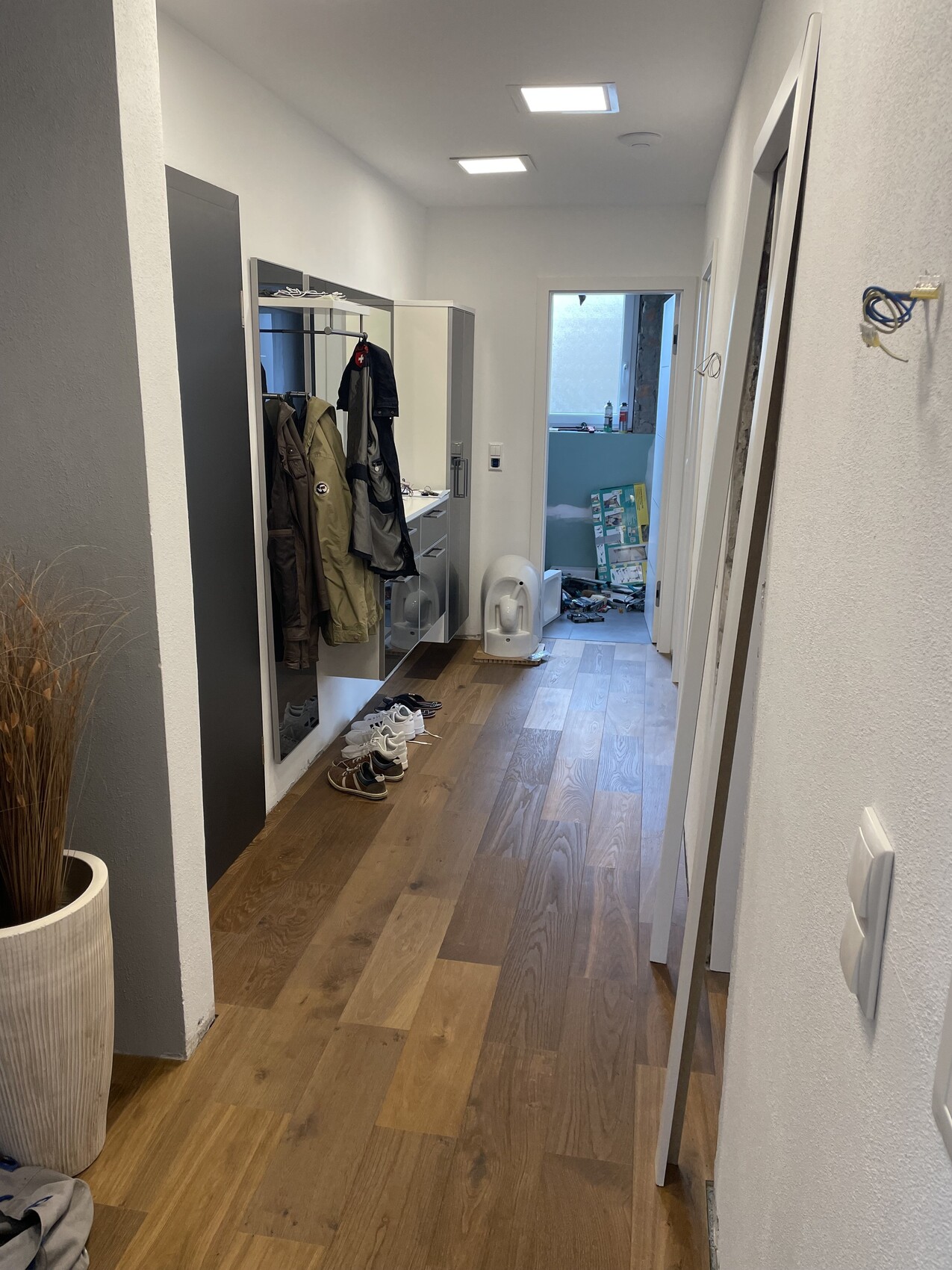 Langer Flur mit Garderobenschrank, Jacken, Schuhe, Spiegel; Tür im Hintergrund.