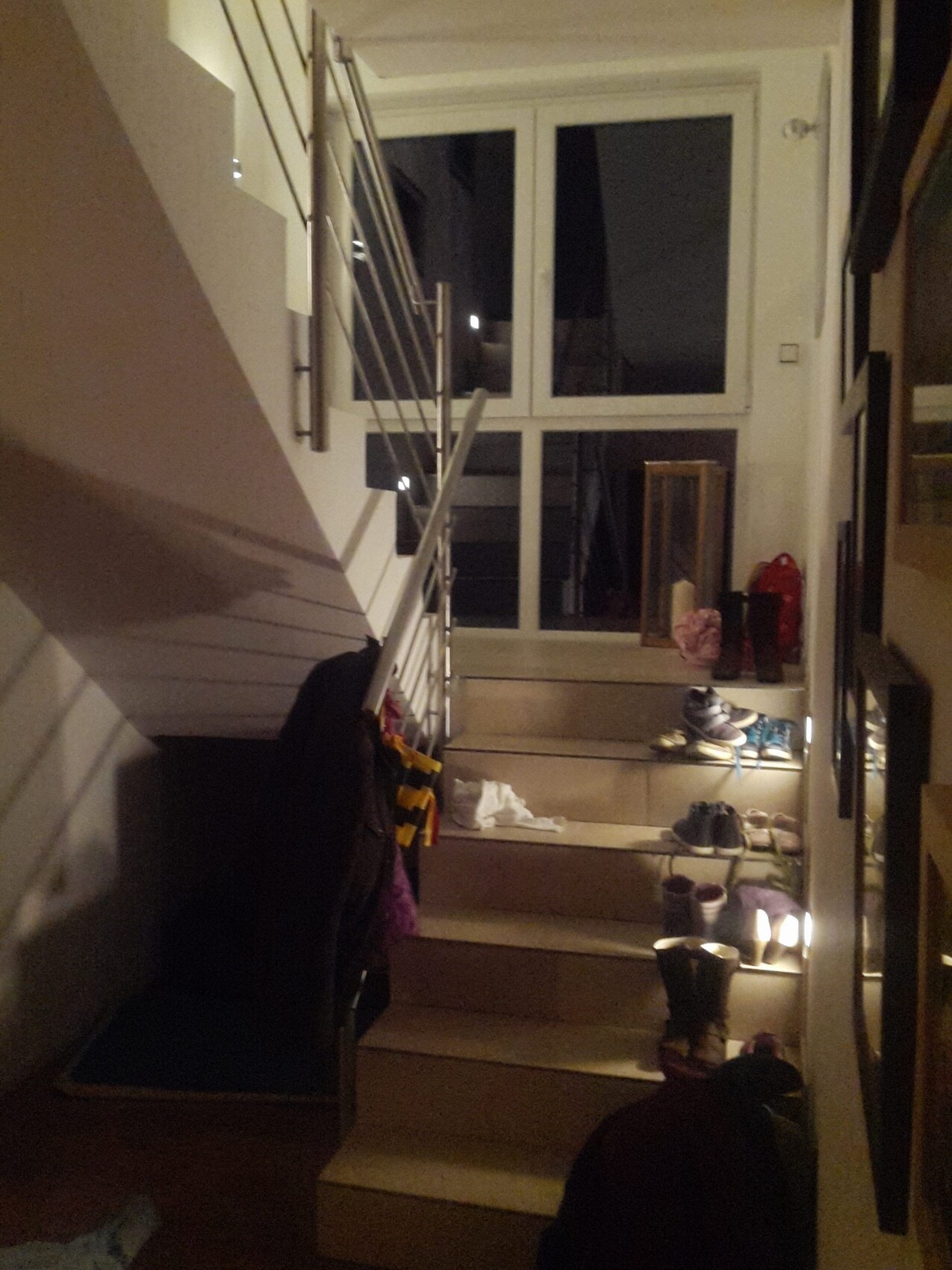 Moderne Treppe im Eingangsbereich mit Metallgeländer, Schuhen und Beleuchtung
