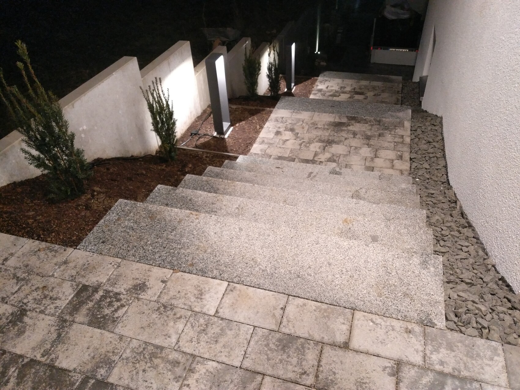 Nachtaufnahme einer modernen Stein-Treppe mit Beleuchtung, Seitenmauern und Kies.