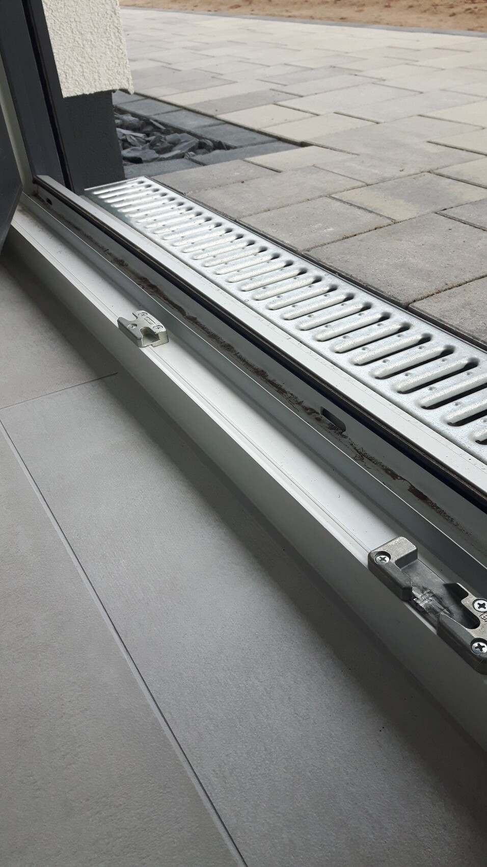 Türschwelle mit gelochter Metallabdeckung; draußen gepflasterter Vorplatz sichtbar.