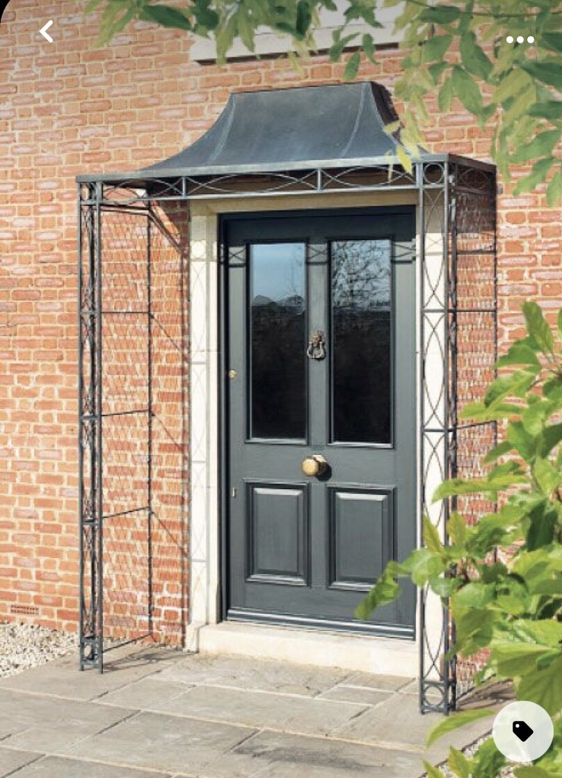 Dunkle Haustür mit Glasfenstern, Eisenrahmen-Überdachung vor rotem Backstein.
