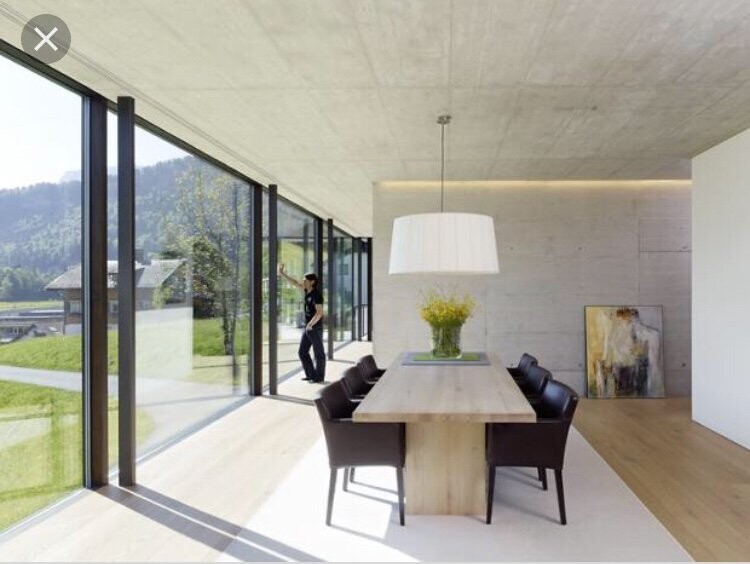 Moderne offene Essecke mit langem Holztisch, schwarzen Stühlen, Glasfront; Person am Fenster.