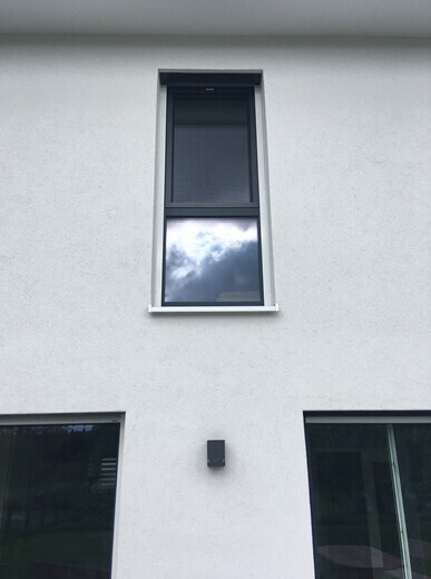 Außenfassade eines Wohnhauses mit Oberfenster, zwei Seitenfenstern und Wandlampe.