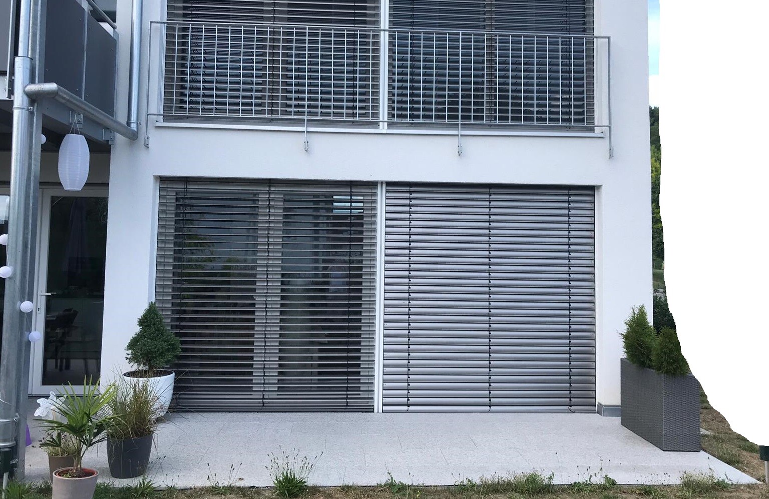 Außenansicht eines modernen Hauses mit Rollläden, Glasfront und Terrasse.
