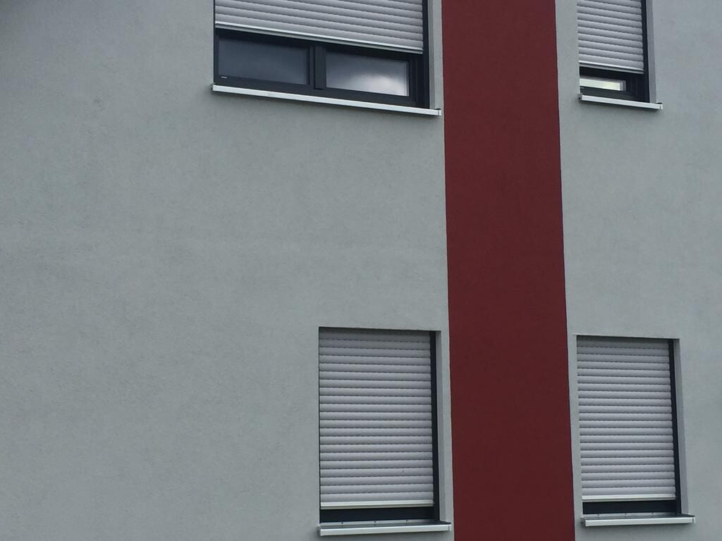Außenansicht eines modernen Gebäudes mit rotem Streifen und Rollladenfenstern