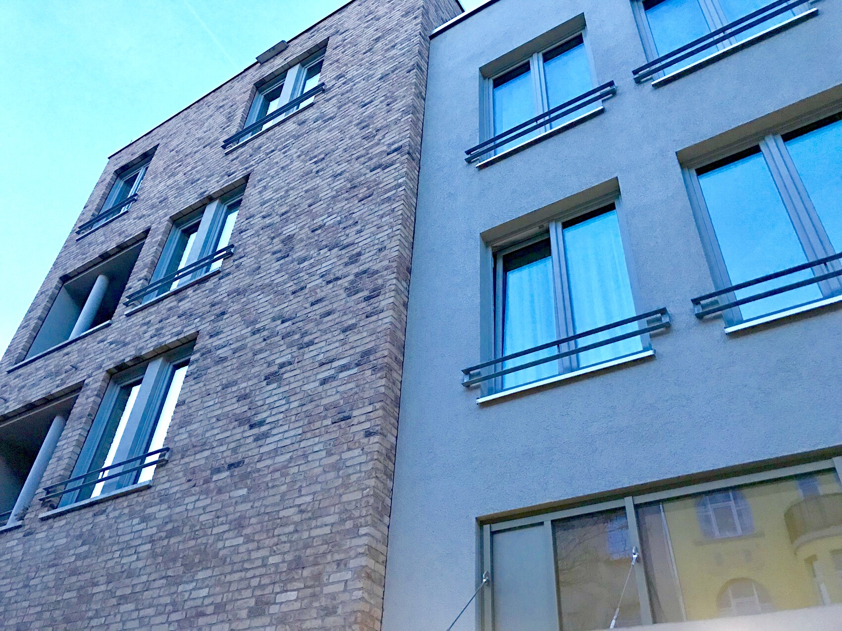 Außenansicht eines modernen Mehrfamilienhauses: Backstein- und Putzfassade mit großen Fenstern.
