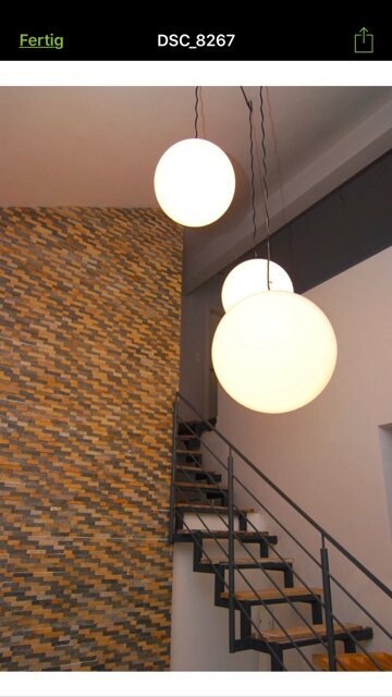 Helle runde Pendelleuchten hängen über einer schwarzen Metalltreppe neben einer Ziegelwand.