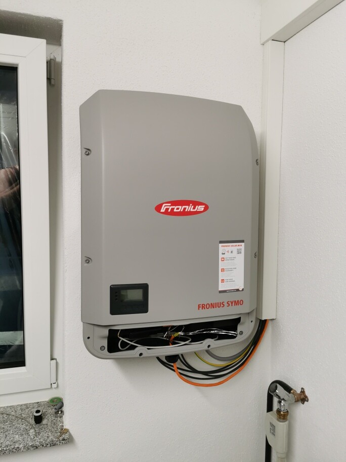 Fronius Symo Solar-Wechselrichter an der Wand mit unten sichtbaren Kabeln.