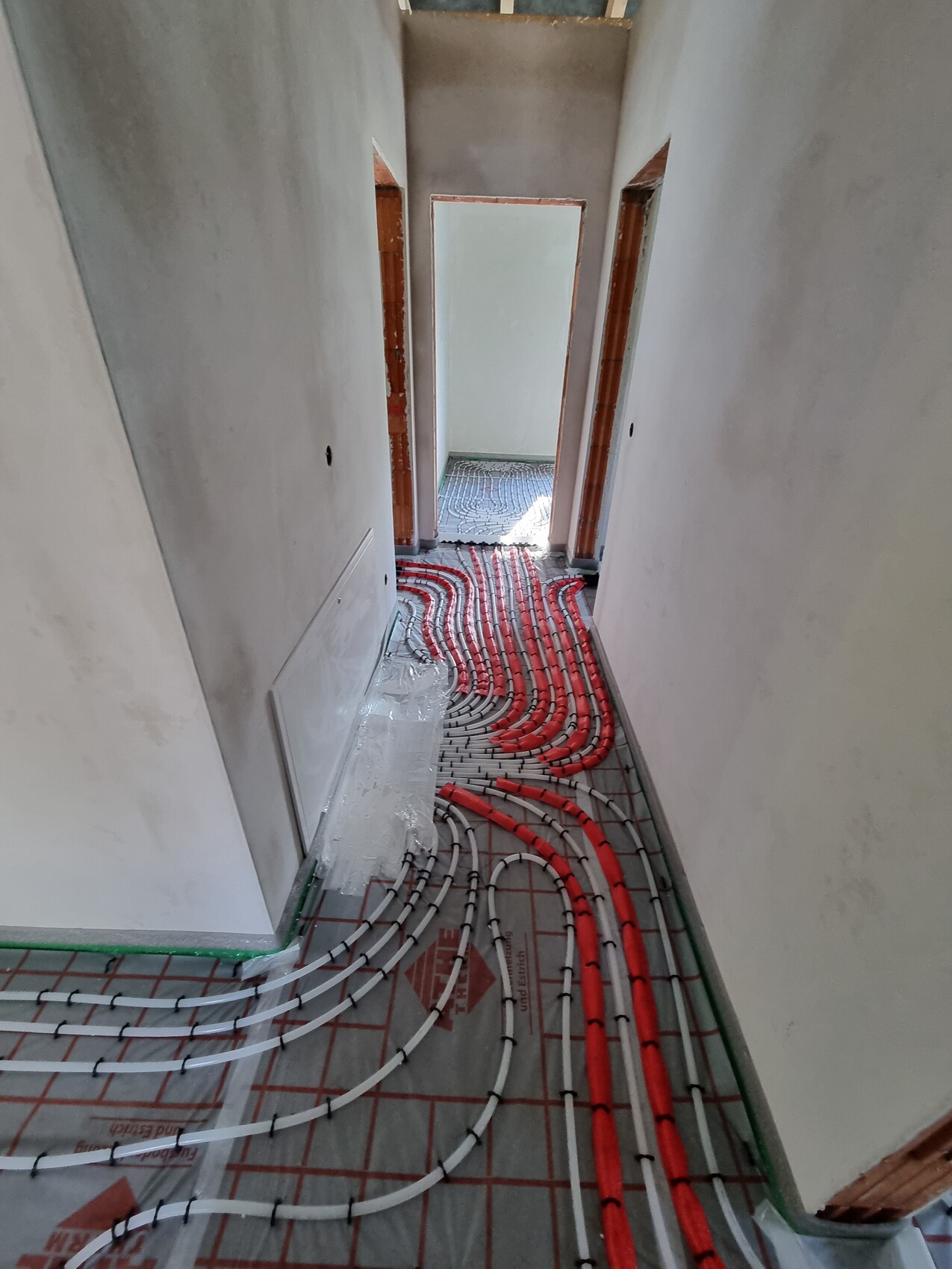 Flur im Bau mit verlegter Fußbodenheizung: rote und weiße Schläuche liegen auf dem Boden.