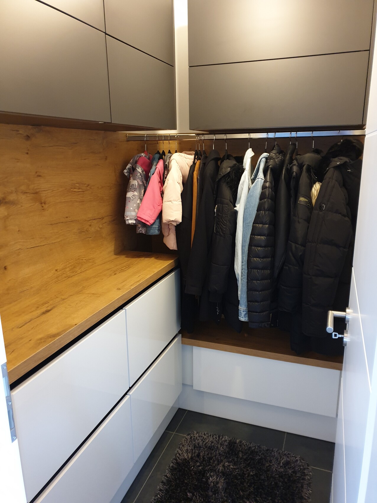 Offener Kleiderschrank mit Mänteln, Jacken, Holzplatte und weißen Schränken.