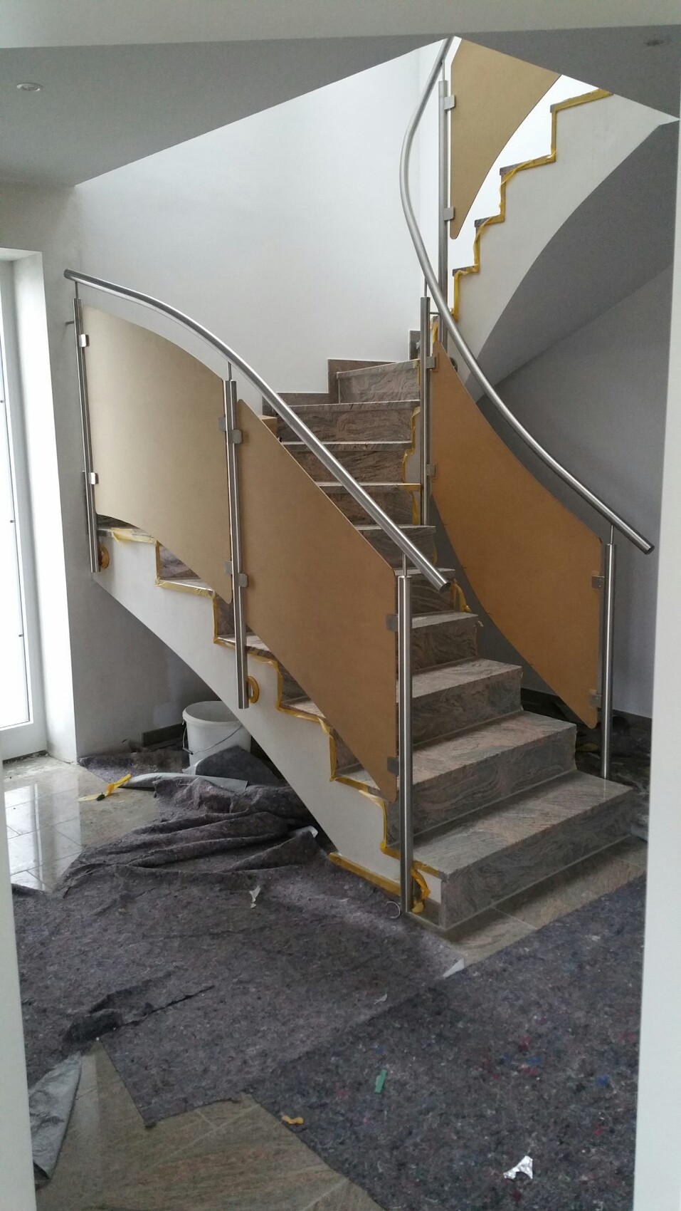 Moderne Wendeltreppe mit Metallgeländern und braunen Seitenpaneele; Baustellenmüll am Boden.