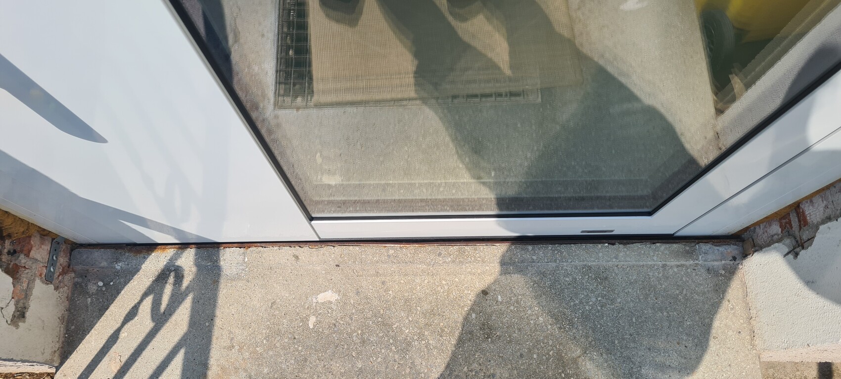 Sicht durch Glasschiebetür auf die Eingangsstufe; Schatten einer Person auf dem Betonboden.