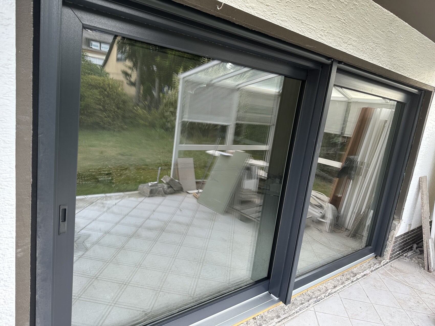 Große dunkelrahmige Schiebetür aus Glas, Blick auf Terrasse und Garten; Baumaterialien davor