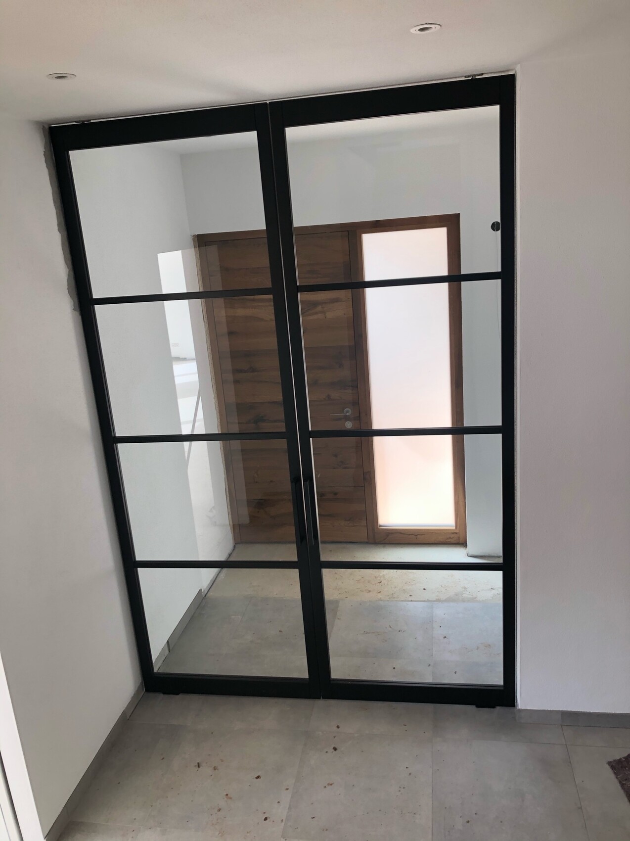 Große Glas-Partition mit schwarzem Metallrahmen und Querstreben im Flur; dahinter Holztür.