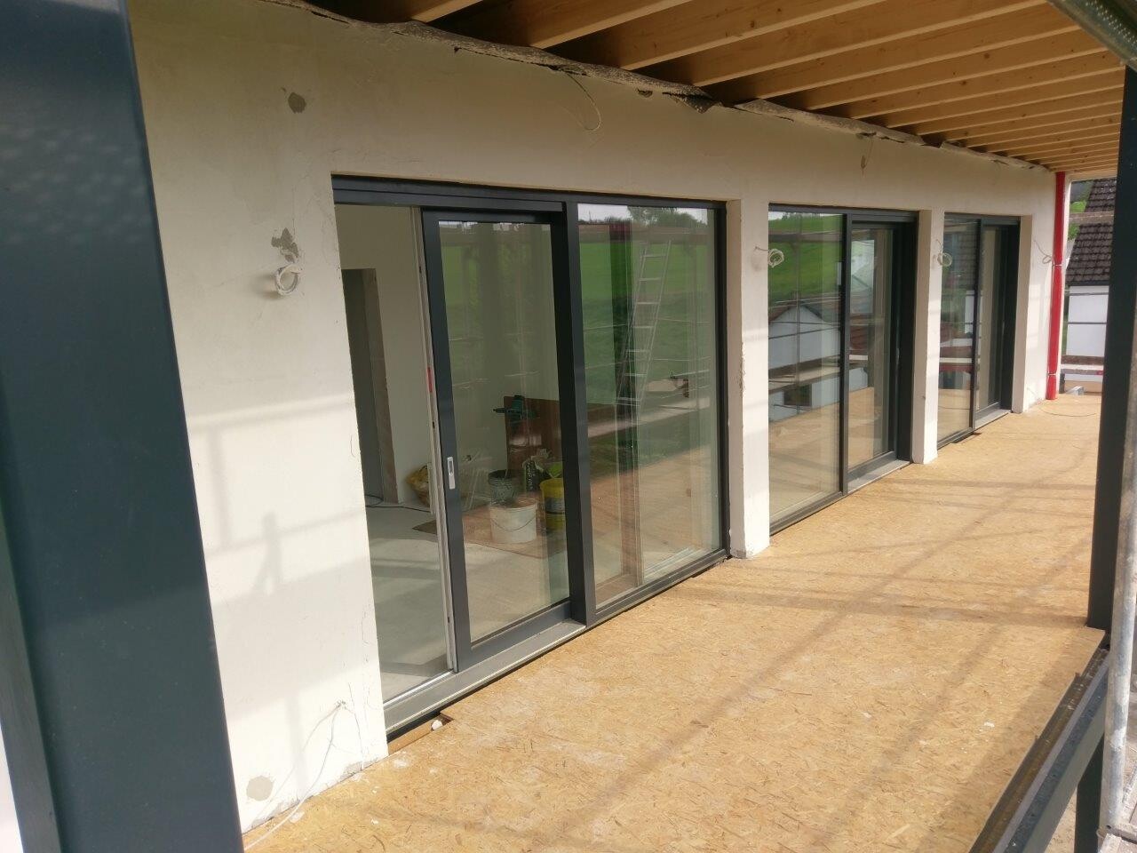 Balkon mit großen Glasschiebetüren, unfertiger Boden und Baugeräte sichtbar.