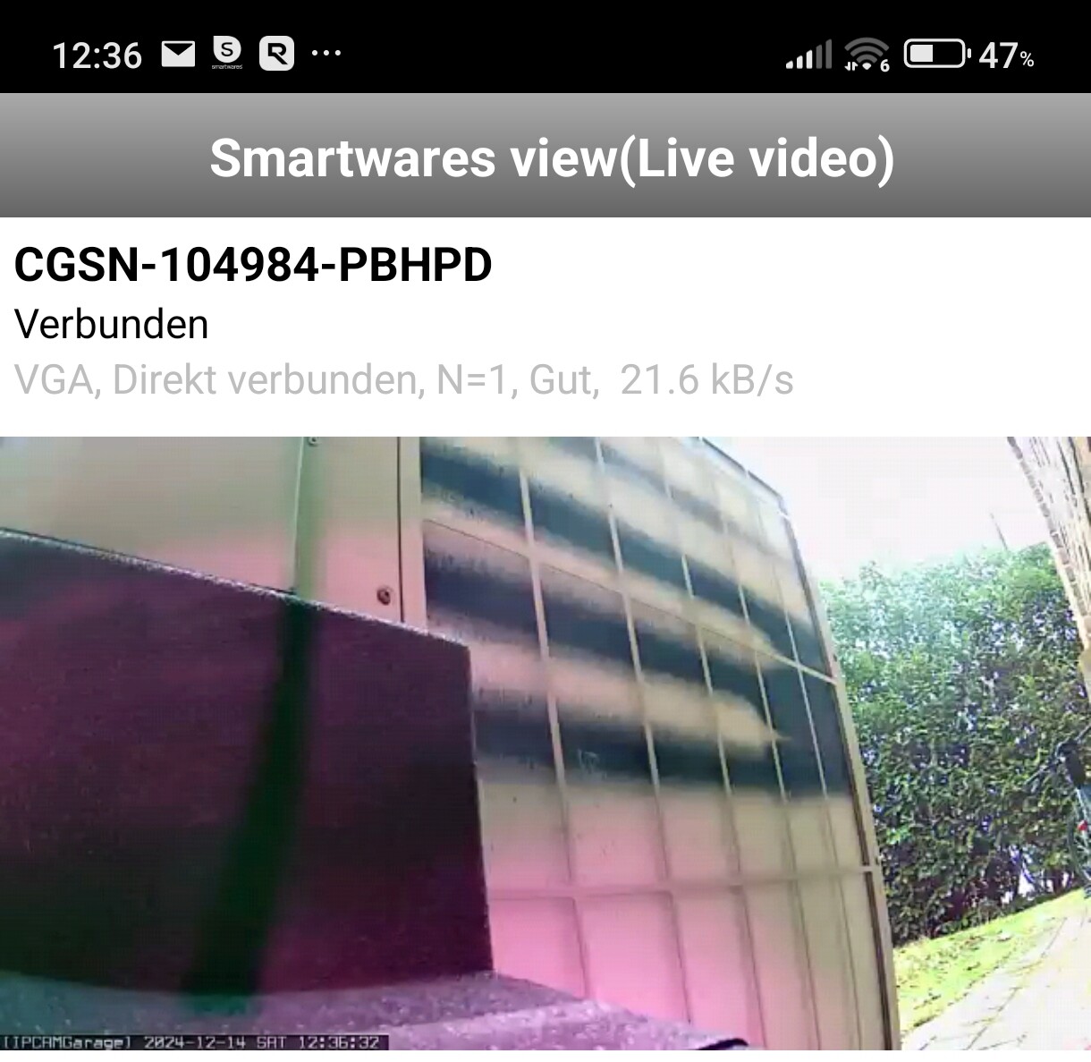 Außenansicht eines Gebäudes mit Glasfassade, dunklem Block links und Bäumen rechts.