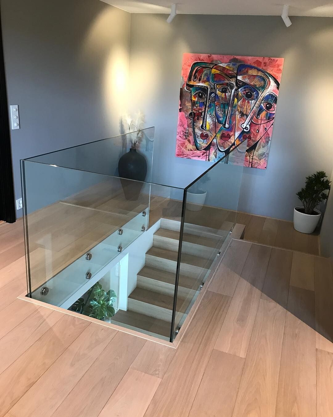 Moderne Treppe mit Glasgeländer; bunte Gesichter-Abstraktmalerei an der Wand, Pflanze.