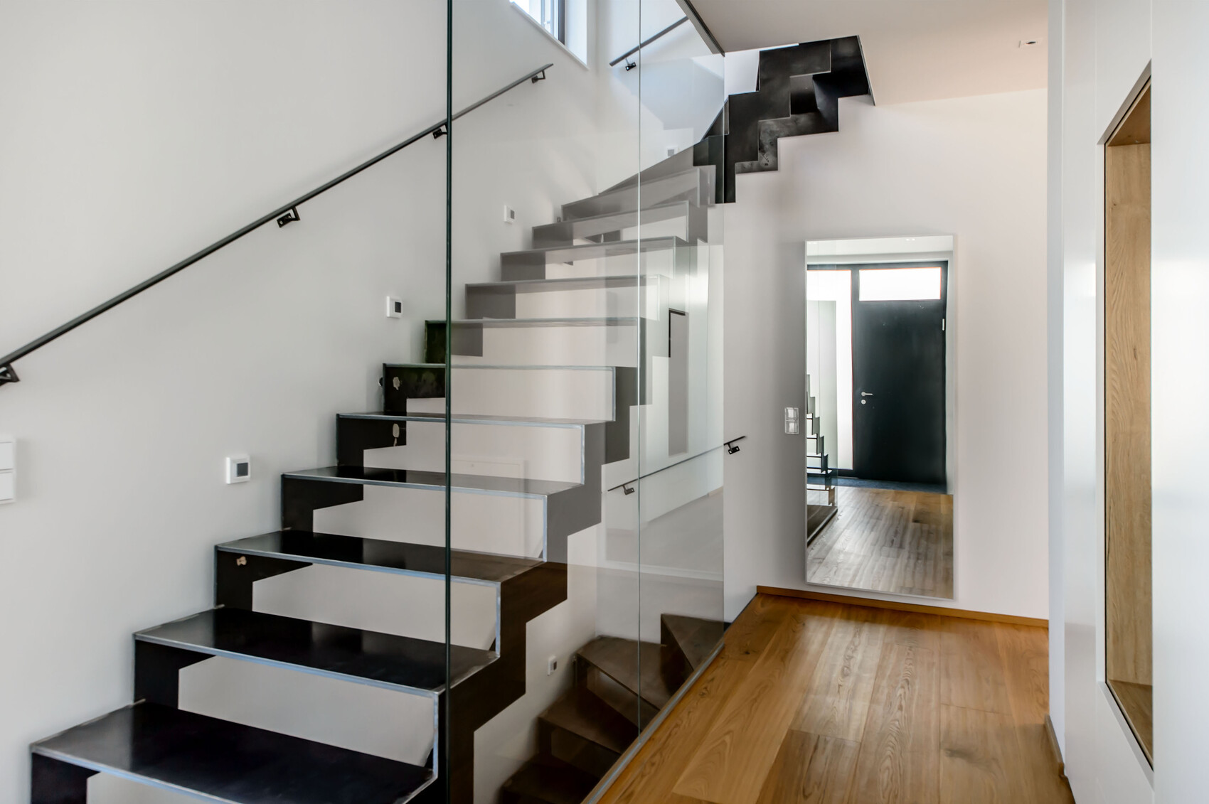 Moderne Glas-Treppenstufen mit Spiegelwand, Holzboden und dunkler Tür im Hintergrund.